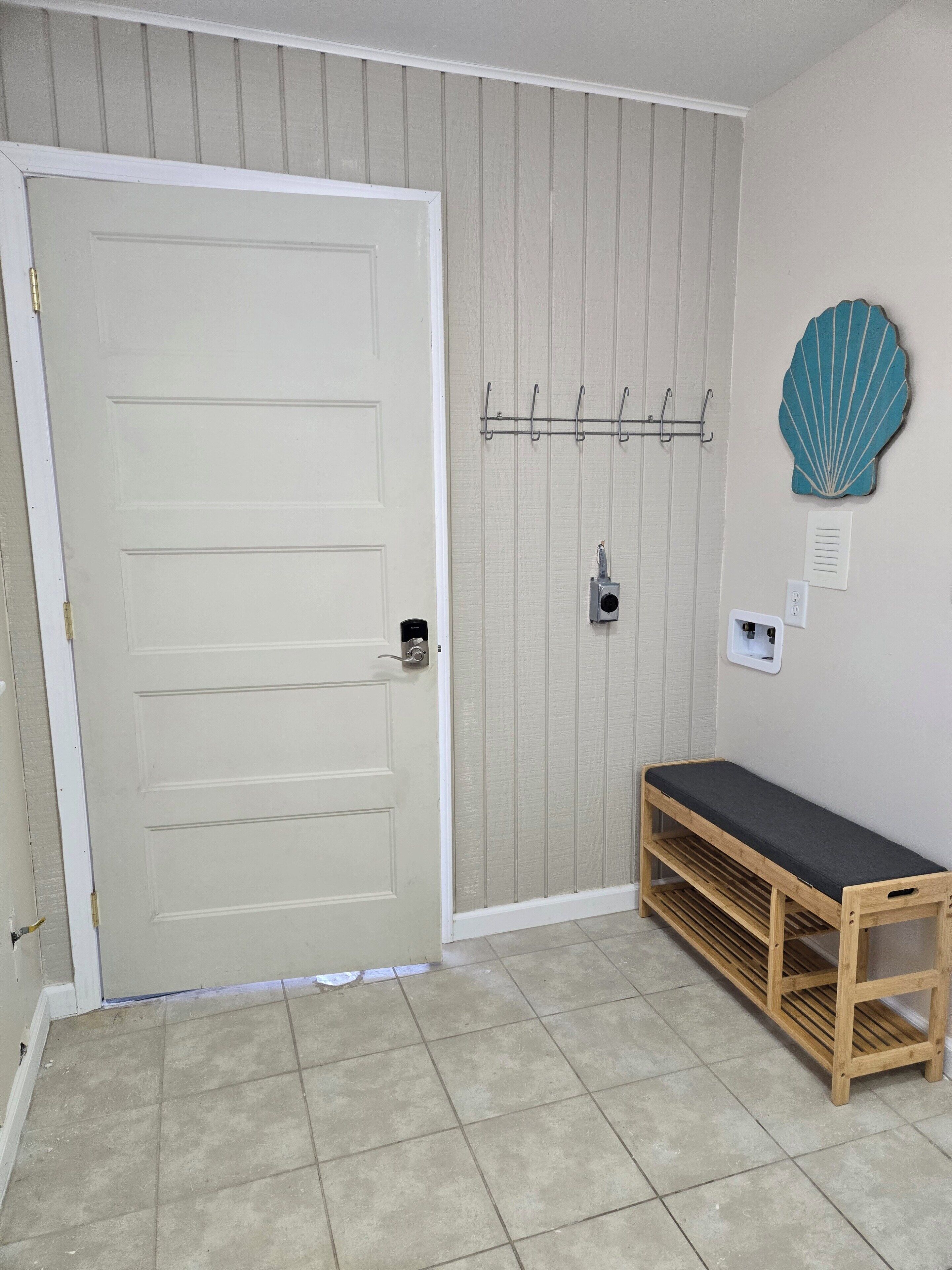 Una habitación con una puerta blanca, un banco, un gancho en la pared y una concha decorativa.