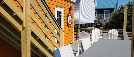 A wooden deck with a ramp leading to a building with a blue roof. There are white chairs and a table on the deck.