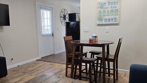Un área de comedor con una mesa y sillas de madera, un televisor montado en la pared, y un letrero que dice 