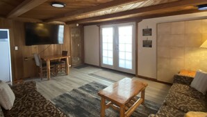 A wooden interior with a sofa, a table, and a TV mounted on the wall. - Historic Lake Roosevelt Home (Kettle Falls)