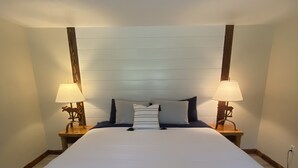 A large bed with white linens, two bedside tables with lamps, and a wooden headboard. - Historic Lake Roosevelt Home (Kettle Falls)