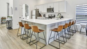 A modern kitchen with white cabinets, a large island with bar stools, stainless steel appliances, and a window with blinds. - Newly renovated pool home - games room - with a secret! (Davenport)