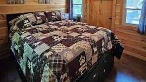 Un dormitorio de cabaña de madera con cama, ventilador de techo y ventanas.