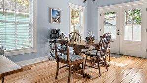 Un comedor con mesa y sillas de madera, cafetera y un cuadro en la pared.