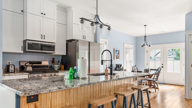 Cocina moderna con armarios blancos, encimera de granito y taburetes de madera.