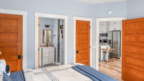Un dormitorio con cama, cómoda y espejo. Hay una puerta que da a un baño y una cocina.