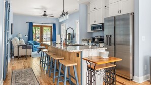 Una cocina moderna con una isla central, electrodomésticos de acero inoxidable y una zona de estar con sofá azul.