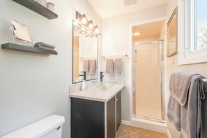 Une salle de bain moderne avec un lavabo en verre, des meubles de rangement aux couleurs sombres et un espace douche.