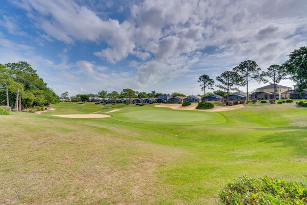 A golf course with a clubhouse, trees, and residential buildings in the background.