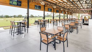 Ein überdachter Außenbereich zum Essen mit Tischen und Stühlen, großen Fenstern und Blick auf einen Golfplatz.