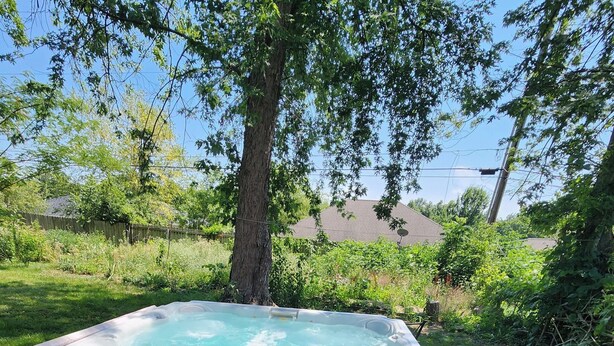 Een hottub in een achtertuin met een houten terras en een boom.