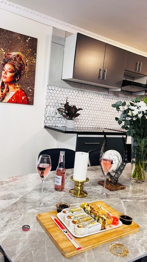 A modern kitchen with a marble countertop, a sushi platter, two wine glasses, and a decorative wall piece. - Clem Guest House (Cape Town)