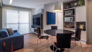 A modern living room with a sofa, a dining table with chairs, a flat-screen TV, and built-in appliances. - Hy Beach Flats - Santa Maria (Recife)