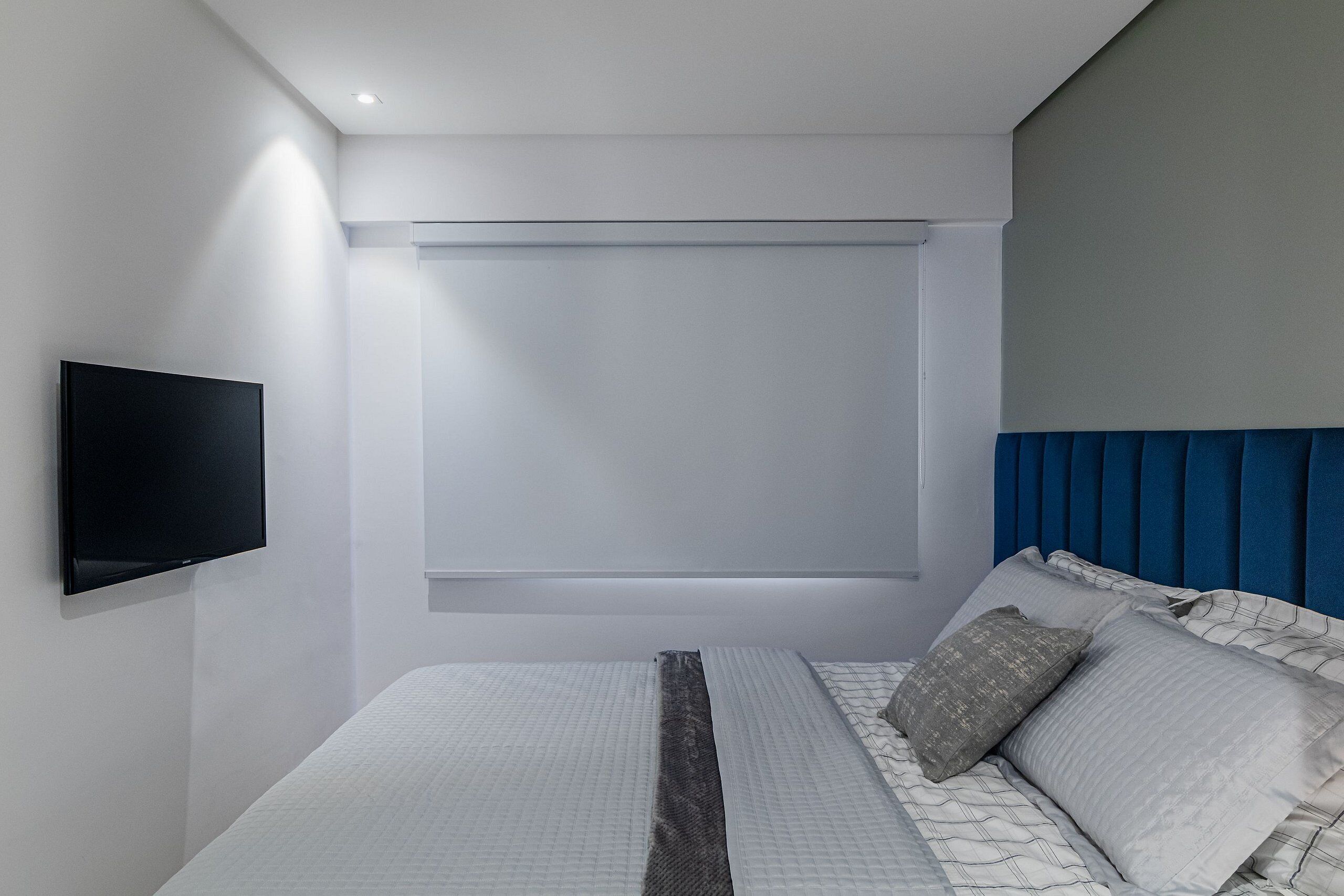 A modern bedroom with a large bed, a mounted TV, and a window with a blind.