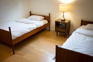 Two single beds with wooden frames and white bedding, a nightstand, and a table lamp.