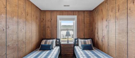 A room with two beds, wooden walls, a star-shaped ceiling light, and a window with a view.