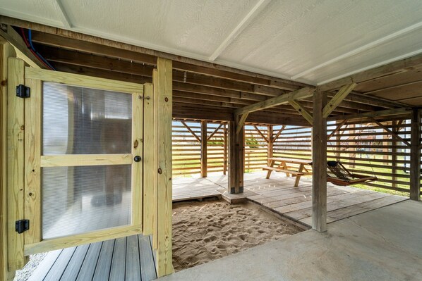 An outdoor wooden deck with a sandy area, a hammock, and a wooden bench.