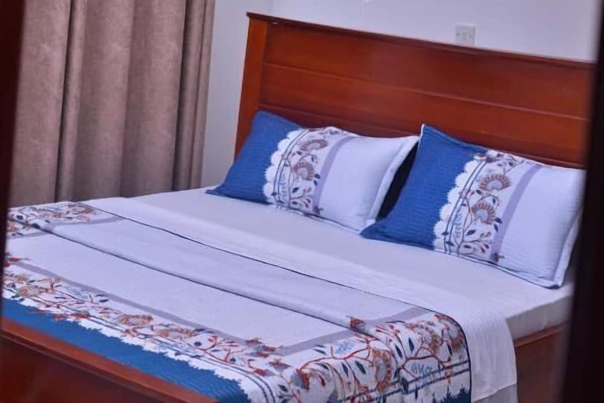 Ein Bett mit Holz-Kopfteil, weißem Baldachin und gemusterten Betttextilien.