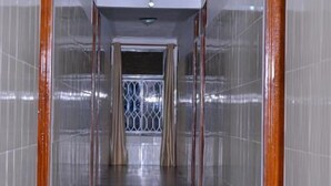 Ein Korridor mit gefliesten Wänden und einem glänzenden Boden, der zu einem Zimmer mit Fenster und Vorhängen führt.
