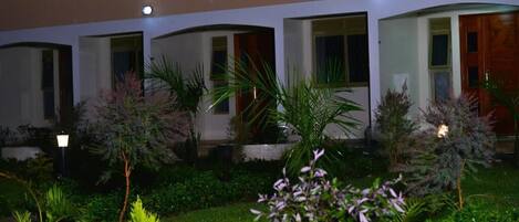 Un hotel con diverse camere, ognuna dotata di porta e finestre. Le camere sono disposte in fila, con un giardino di fronte.