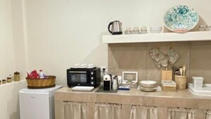 Une cuisine compacte équipée d’un réfrigérateur, d’un four à micro-ondes et d’une machine à café sur le plan de travail, d’un sol à motifs et d’un luminaire suspendu.
