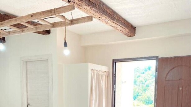 Un coin repas avec une table en bois et des chaises blanches, un sol à motifs et une vue sur l’extérieur par une porte ouverte.