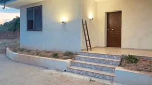 Une maison avec une seule porte, un petit porche avec des marches et une échelle appuyée contre le mur.