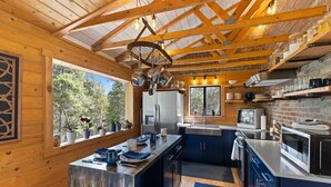 A modern kitchen with wooden beams, a large island, and a view of the outdoors. - Enjoy the Now in an Alpine Oasis (Alma)