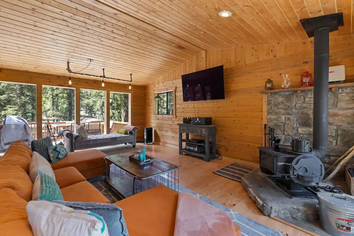 A cozy cabin interior with a stone fireplace, wooden walls, a sofa, and a television mounted on the wall.