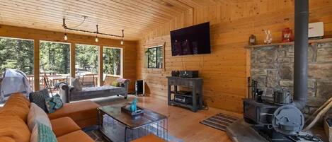 A cozy cabin interior with a stone fireplace, wooden walls, a sofa, and a television mounted on the wall.