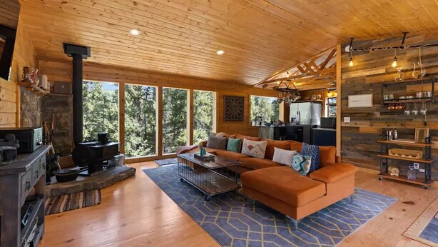 A cozy cabin interior with a wooden ceiling, a stone fireplace, a sofa, and a kitchen area. - Enjoy the Now in an Alpine Oasis (Alma)