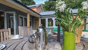 A wooden table with a stainless steel kettle, a green vase with white flowers, and a wicker basket. - Church Farm Barn (Saxmundham)