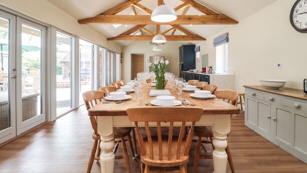 A dining area with a long wooden table set for a meal, surrounded by chairs. - Church Farm Barn (Saxmundham)