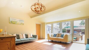 A spacious living room with two sofas, a wooden cabinet, and large windows offering a view of the outside. - Church Farm Barn (Saxmundham)