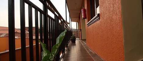A corridor with a black metal railing, a potted plant, and a red fire extinguisher on the wall.