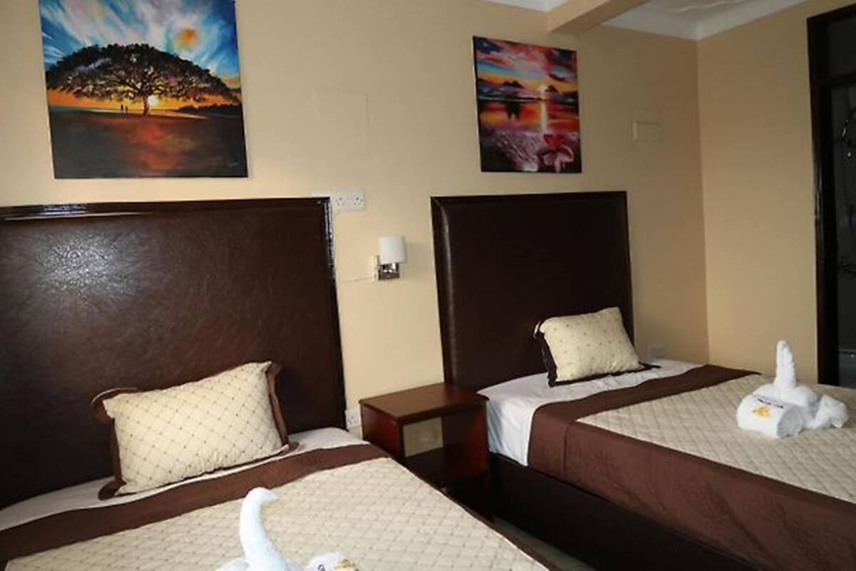 A hotel room with two beds, each with a brown headboard, a nightstand, and a painting on the wall.