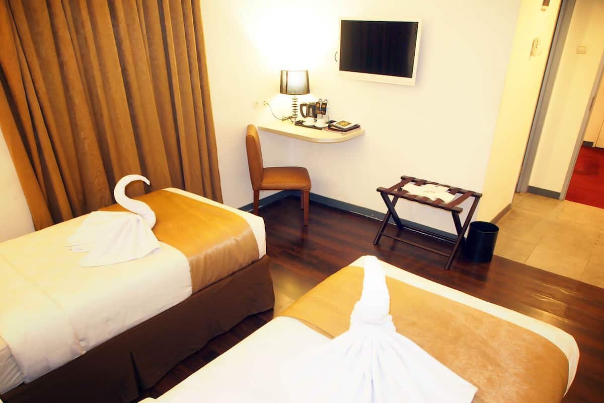 A hotel room with two beds, a desk, a chair, and a television.