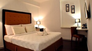 A hotel room with a large bed, two bedside lamps, a small desk with a chair, and framed pictures on the wall. - MV Orienchi (Jakarta)