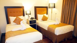 Two adjacent hotel beds with matching headboards, a bedside table with a lamp, and a wooden floor. - MV Orienchi (Jakarta)