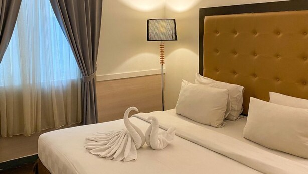 A hotel room with a large bed, a headboard, and a window with curtains. - MV Orienchi (Jakarta)