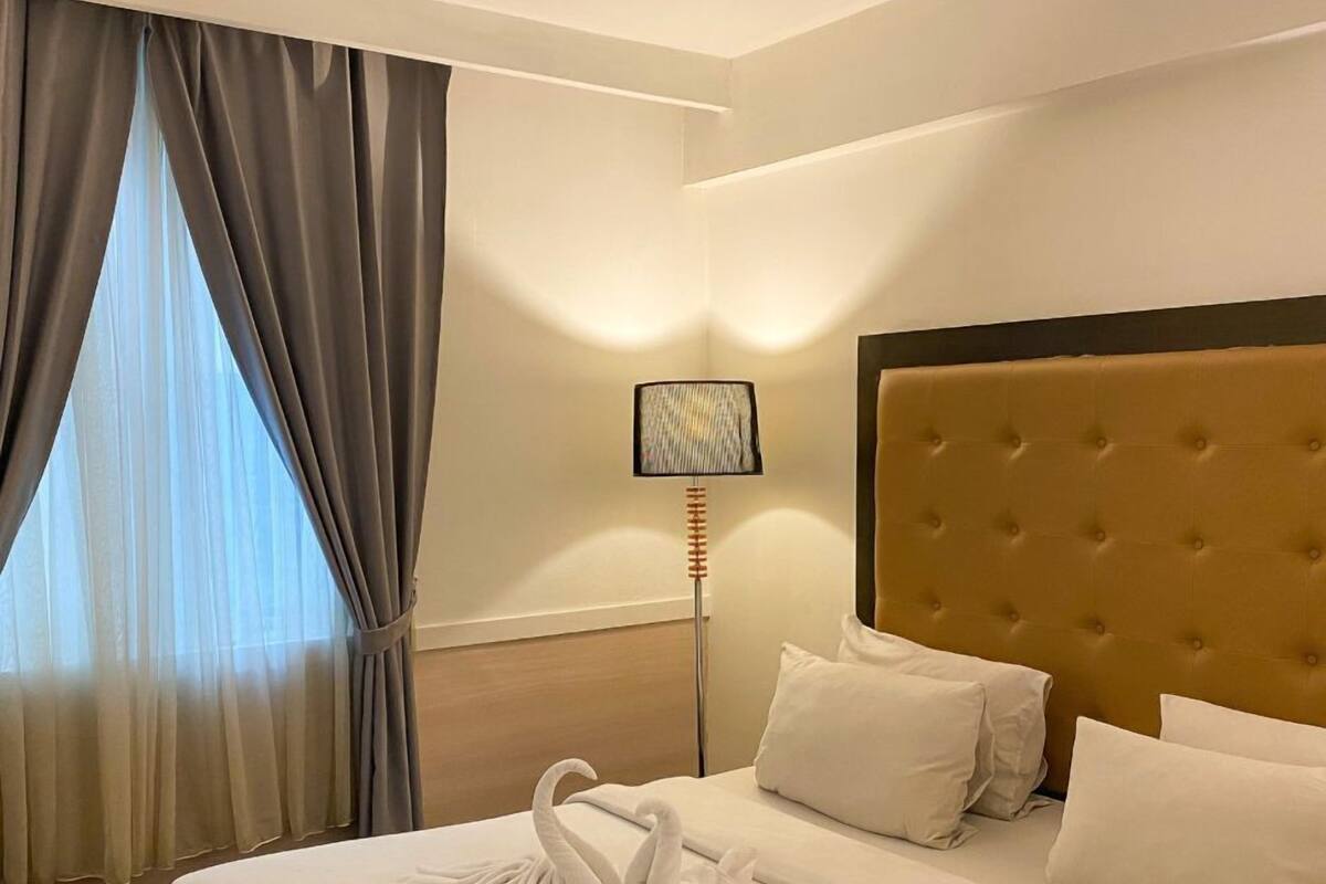 A hotel room with a large bed, a headboard, and a window with curtains.