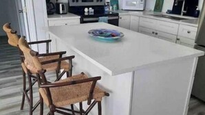 A modern kitchen with white cabinets, a central island with bar stools, a microwave, a stove, and a sink. - Sea Biscuit Ocean Villa 911 (Abaco)