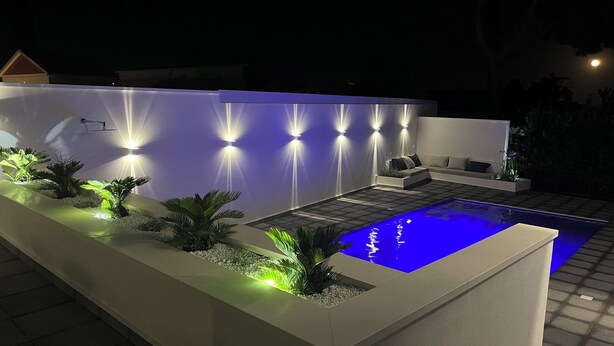 Un espace piscine extérieur moderne au design minimaliste, comprenant un long bac à plantes et un coin salon avec un canapé et une table basse.