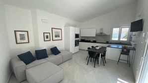 Un appartement moderne avec un canapé gris, une table à manger avec des chaises, un coin cuisine et des tableaux encadrés au mur.