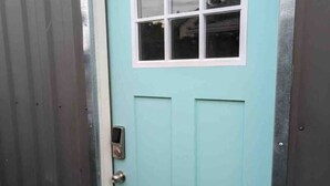 Een blauwgroene deur met een klein raam en een deurbel.