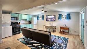 Een compacte keuken met moderne apparaten, een eethoek met een televisie, en een gezellige zithoek met een bank en een klein tafeltje.