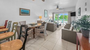Un vaste espace de vie comprenant un coin repas avec une table, des chaises et un ventilateur de plafond. Une grande fenêtre offre une vue sur la verdure environnante.