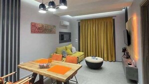 Una sala de estar moderna con comedor, que incluye un conjunto de sofá, una mesa de centro y un televisor montado en la pared.