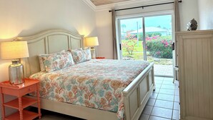 Une chambre à coucher comprenant un lit, deux lampes de chevet, une table de chevet et une vue sur un jardin, accessible par une porte-fenêtre coulissante.