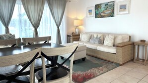 Un salon comprenant une table à manger, des chaises, un canapé et un tapis. Deux tableaux ornent le mur et une lampe se trouve sur une table d’appoint.
